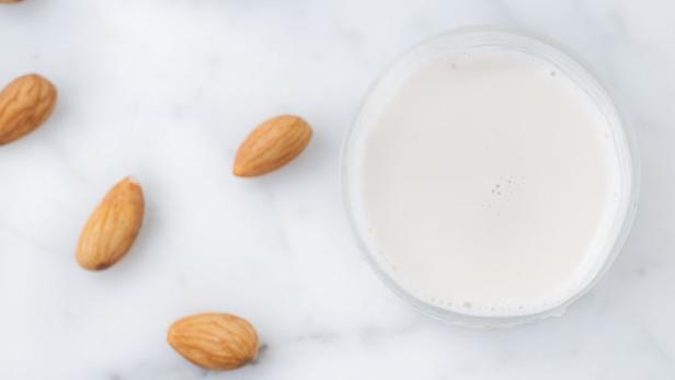 Ein Glas Mandelmilch steht neben Mandeln auf einer Marmoroberfläche.