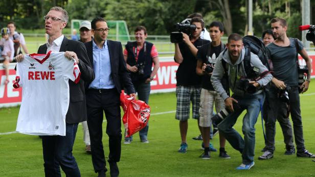 Der neue Cheftrainer des 1. Fc Köln, Peter Stöger (l), geht am 14.06.2013 in Köln (Nordrhein-Westfalen) mit einem Trikot in der Hand über den Trainingsplatz. Der 1. FC Köln hat Peter Stöger in Köln vorgestellt. Foto: Oliver Berg/dpa +++(c) dpa - Bildfunk+++