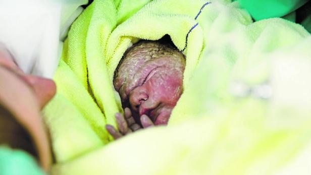 Newborn baby wrapped in blankets after birth. Mother looking for the first time on new born daughter