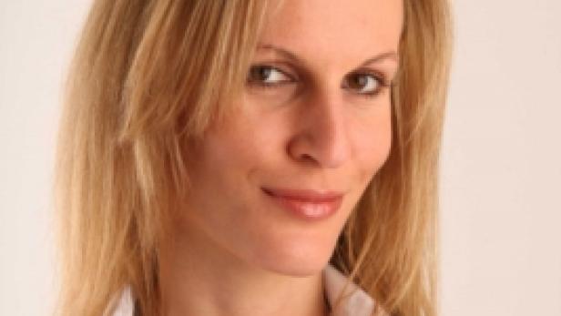 Eine blonde Frau mit weißem Hemd und einer Halskette lächelt.