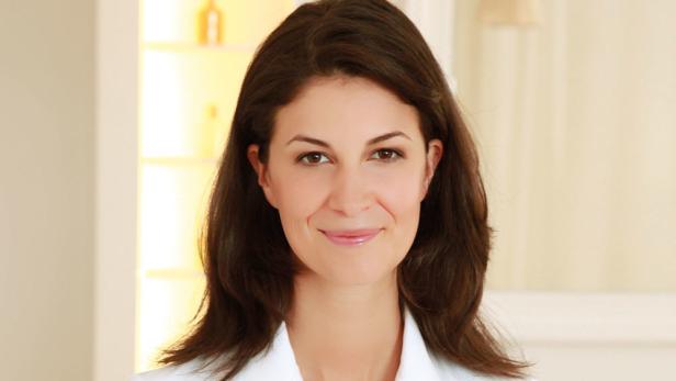 Eine lächelnde Frau mit braunen Haaren und einem weißen Oberteil.