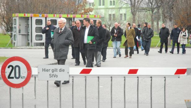 Eine Gruppe von Menschen geht hinter einer Schranke mit einem 20 km/h-Schild entlang.