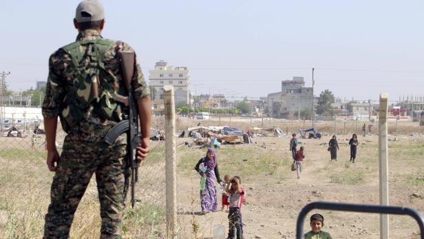 Ein Soldat mit Gewehr bewacht ein Flüchtlingslager am Stadtrand.