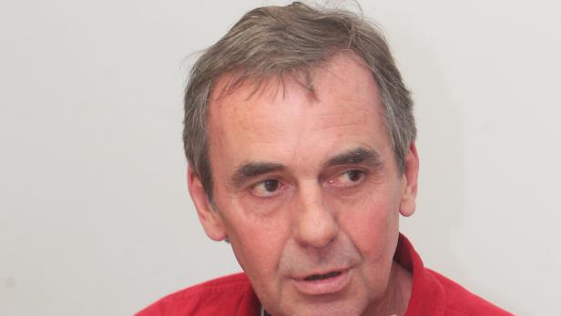 Porträt eines Mannes mit grauem Haar und rotem Hemd.