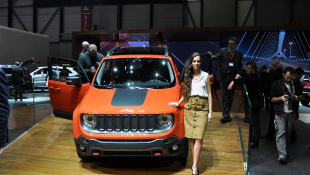 Eine Frau posiert vor einem orangefarbenen Jeep auf einer Automobilmesse.