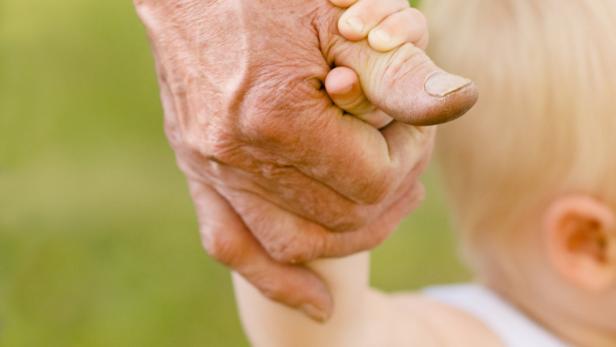 Die Hand eines älteren Menschen hält den Finger eines kleinen Kindes.