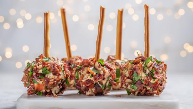 Käsebällchen mit Speck, Kräutern und einem Salzstangenstiel auf einem Brett.