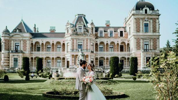 Ein Brautpaar steht vor einem Schlossgarten mit großem Schloss.