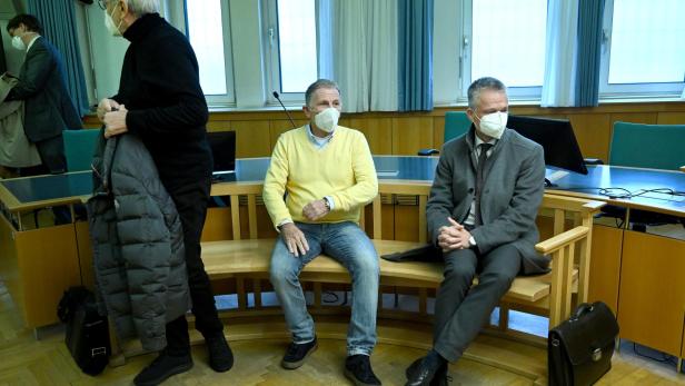 Drei Männer mit Gesichtsmasken sitzen in einem Gerichtssaal.