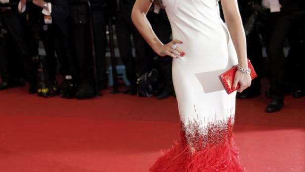 Cheryl Cole posiert in einem weißen Kleid mit roter Federboa auf dem roten Teppich für Fotografen.
