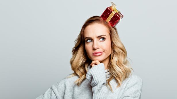 Eine Frau mit einem kleinen, roten Geschenk auf dem Kopf schaut nachdenklich zur Seite.