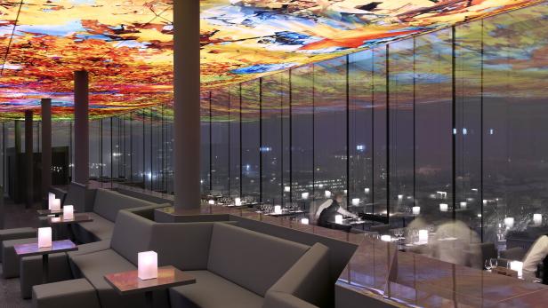 Ein Restaurant mit farbenfroher Deckenkunst und Blick auf eine Stadt bei Nacht.