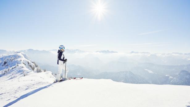 Eine Skifahrerin genießt die Aussicht auf die verschneiten Berge an einem sonnigen Tag.