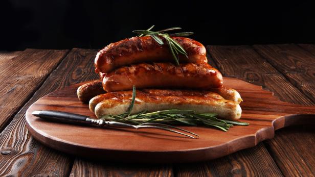 Mehrere gegrillte Würstchen sind auf einem Holzbrett mit Rosmarin angerichtet.