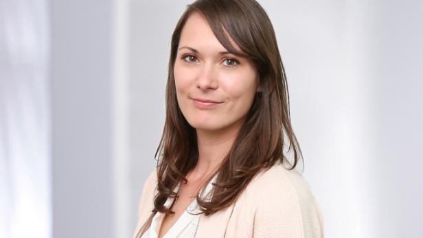 Porträt einer lächelnden Frau mit braunen Haaren und einem hellen Blazer.
