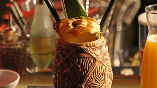 Ein exotischer Cocktail in einem Tiki-Becher, garniert mit einer Physalis und einem Blatt.