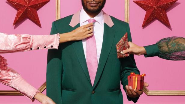 Ein Mann im grünen Anzug wird mit Accessoires und einem Geschenk ausgestattet.