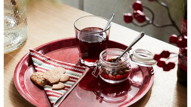 Ein rotes Tablett mit Keksen, einem Glas Saft und einem Glas mit Nüssen und Beeren.
