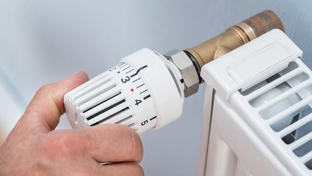 Person dreht am Thermostat des Heizkörpers