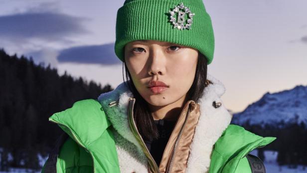 Eine Frau mit grüner Mütze und Jacke vor einer verschneiten Berglandschaft.