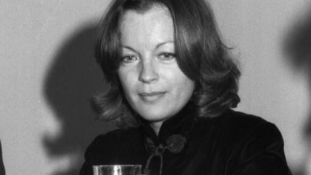 Romy Schneider Schwarzweißporträt von Romy Schneider an einem Tisch mit Mikrofon und Wasserglas.