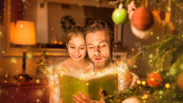 Ein Vater liest seiner Tochter zu Weihnachten zu Hause aus einem Buch vor.