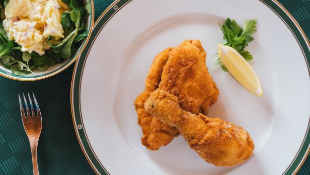 Ein Teller mit paniertem Hähnchen und einer Zitronenspalte, dazu Kartoffelsalat mit Feldsalat.