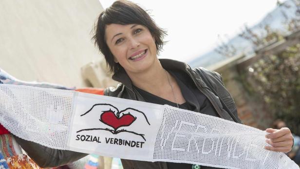Eine Frau hält ein Schild mit der Aufschrift „Sozial verbindet“ und einem roten Herz.