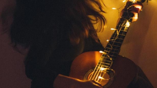 Eine Person hält eine mit Lichtern dekorierte Gitarre im Dunkeln.