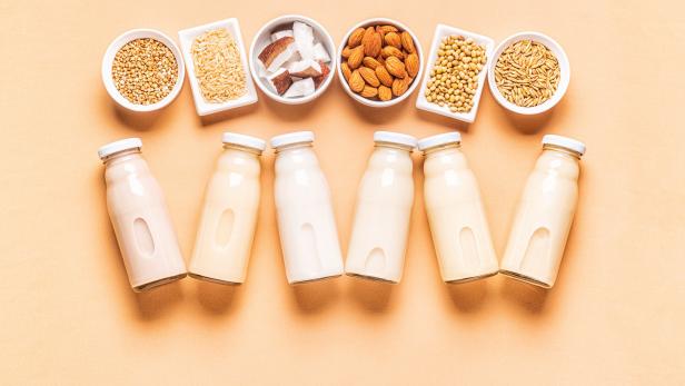 Verschiedene Milchalternativen in Glasflaschen und Schüsseln mit Zutaten wie Mandeln und Sojabohnen.