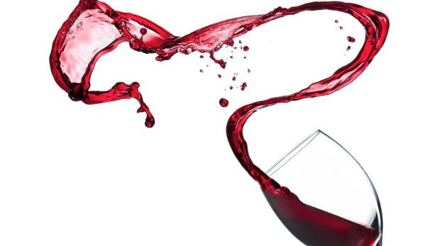 Rotwein spritzt aus einem Glas vor einem weißen Hintergrund.