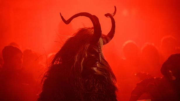 Ein Krampus mit Hörnern und Fellkostüm steht im roten Licht.