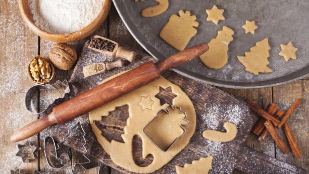 Auf einem Holztisch liegen Teig, Ausstechformen und Zutaten für Weihnachtsplätzchen.