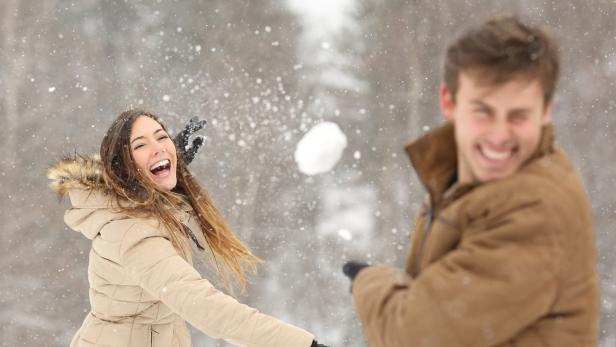 Ein Mann und eine Frau werfen sich im Schnee Schneebälle zu.