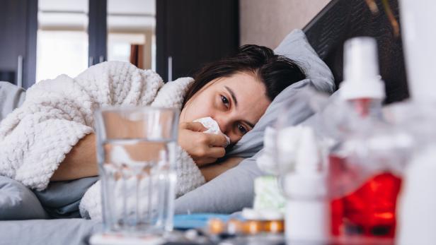 Eine kranke Frau liegt im Bett und putzt sich die Nase. 