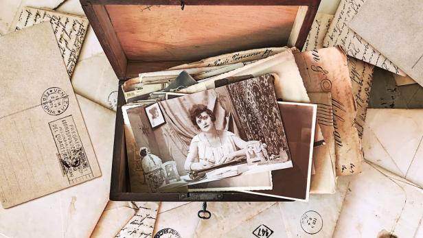 Eine offene Holzkiste ist gefüllt mit alten Briefen und einem Schwarzweißfoto einer Frau.