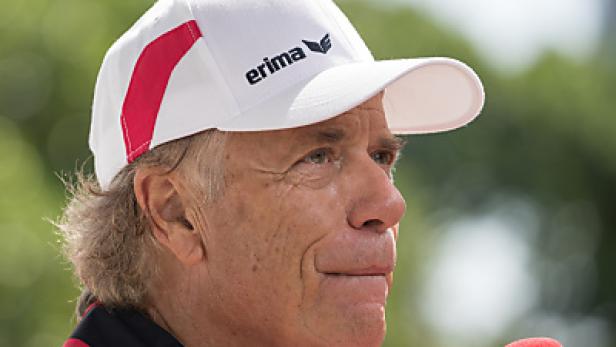 Ein Mann mit einer weißen Erima-Kappe spricht in ein rotes Mikrofon.