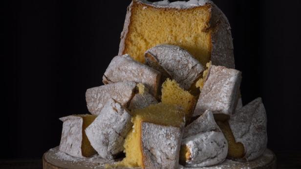 Ein angeschnittener, mit Puderzucker bestäubter Pandoro auf einem Holzbrett.