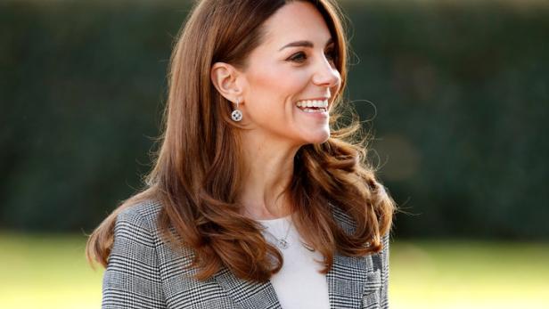 Catherine, Prinzessin von Wales, lächelt in einem karierten Blazer und einer roten Hose.