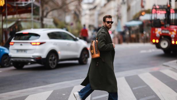 Ein Mann mit Sonnenbrille und Rucksack überquert eine Straße.