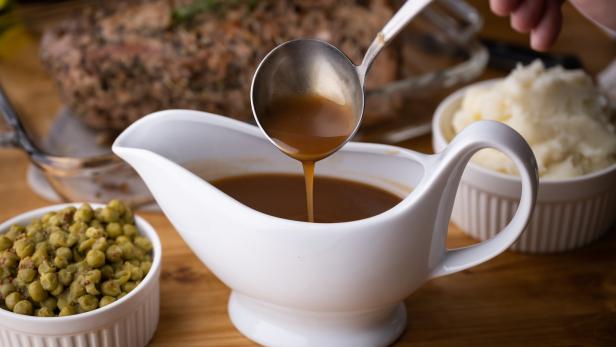 Soße wird in eine weiße Soßenschüssel gegossen, mit Beilagen wie Erbsen und Kartoffelpüree.