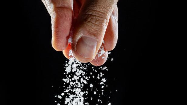 Eine Hand streut grobes Salz vor einem schwarzen Hintergrund.