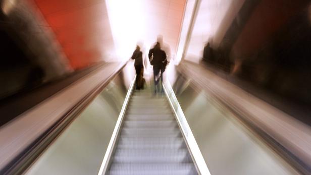 Zwei Personen fahren mit einer Rolltreppe nach oben.