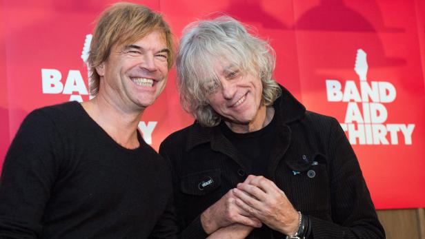Bob Geldof und ein weiterer Mann posieren vor einem „Band Aid Thirty“-Plakat.