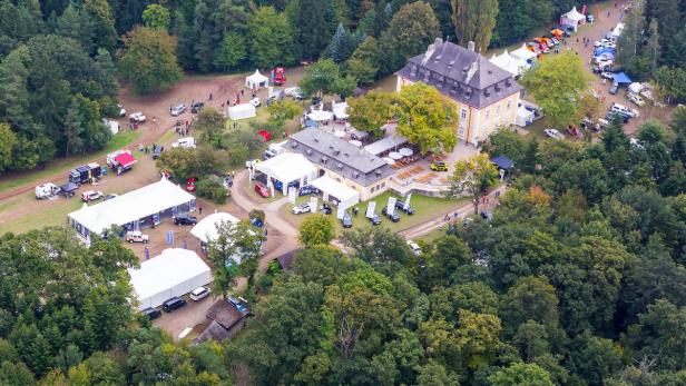 Luftaufnahme eines Anwesens mit einem Herrenhaus, Zelten und geparkten Autos inmitten eines Waldes.