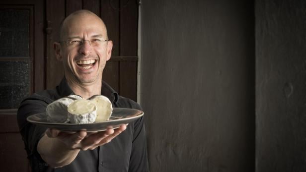 Ein lachender Mann präsentiert eine Käseplatte.