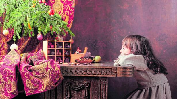 Little girl is waiting for Christmas in front of a vintage table with sweets, spices and toys .