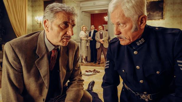 Zwei Männer, ein Detektiv und ein Polizist, untersuchen einen Tatort.