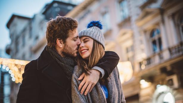 Ein Mann küsst eine lächelnde Frau mit Mütze auf die Wange.