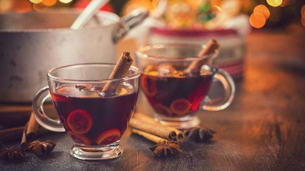 Zwei Tassen Glühwein mit Zimtstangen und Orangenscheiben auf einem Tisch.